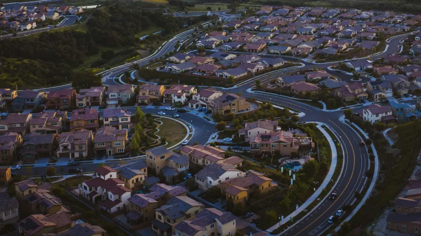 Aerial view of a suburban neighborhood with winding roads and rolling green hills under a dramatic evening sky.